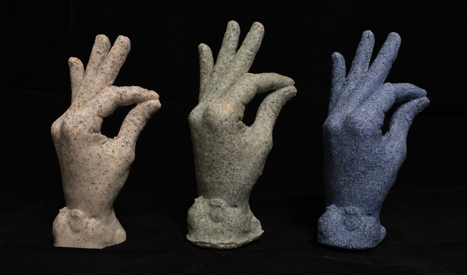 three casts of female hand with a granite look: black, blue, green