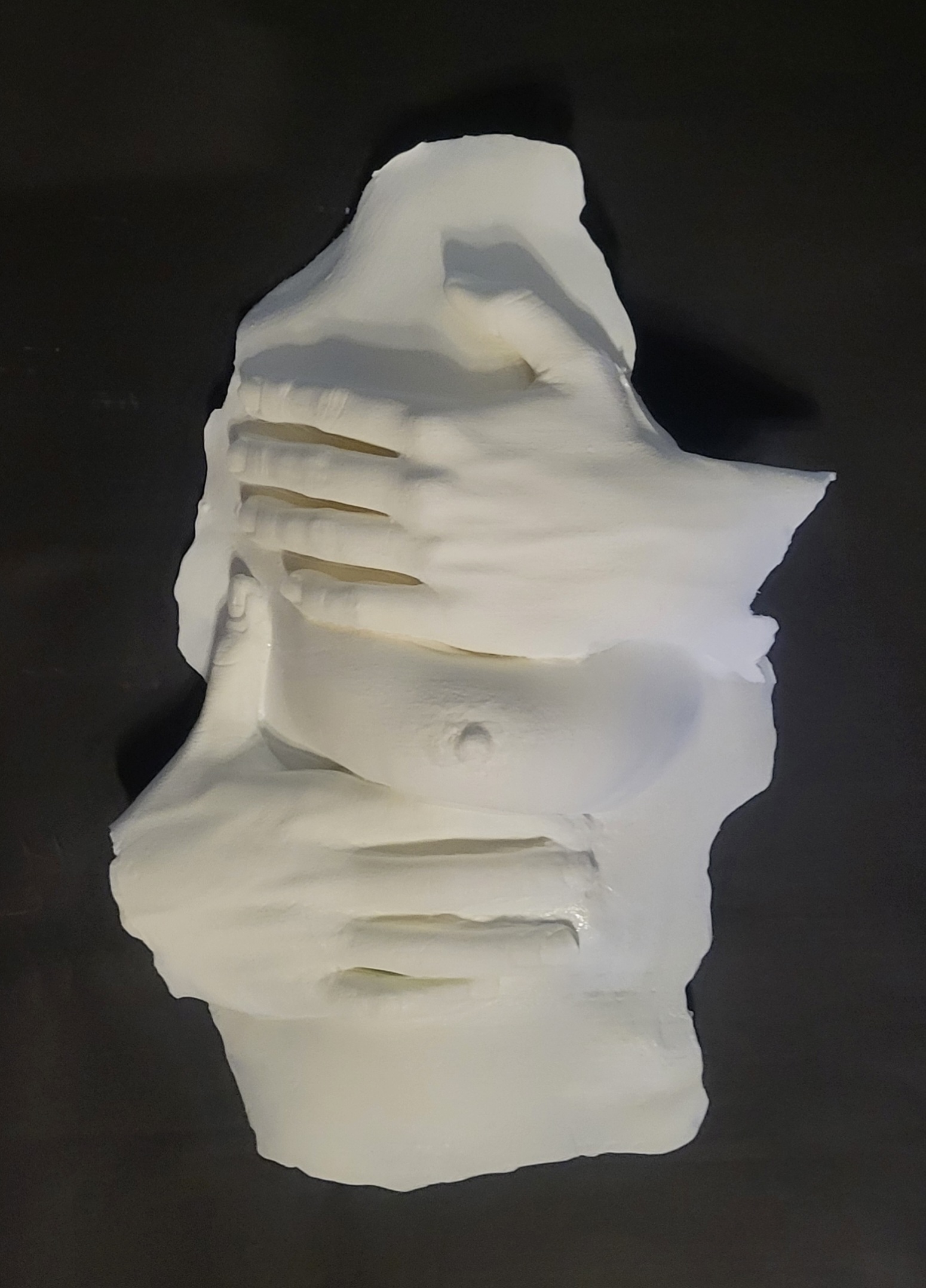 white plastic casting of woman's left breast with her left hand above it and right hand below it